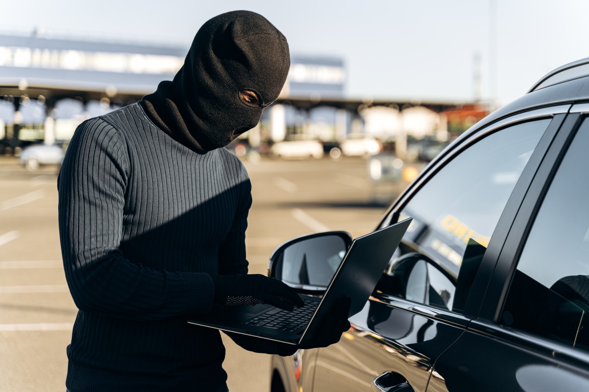 Car thief with laptop hacking alarm system while standing near the car at the daytime