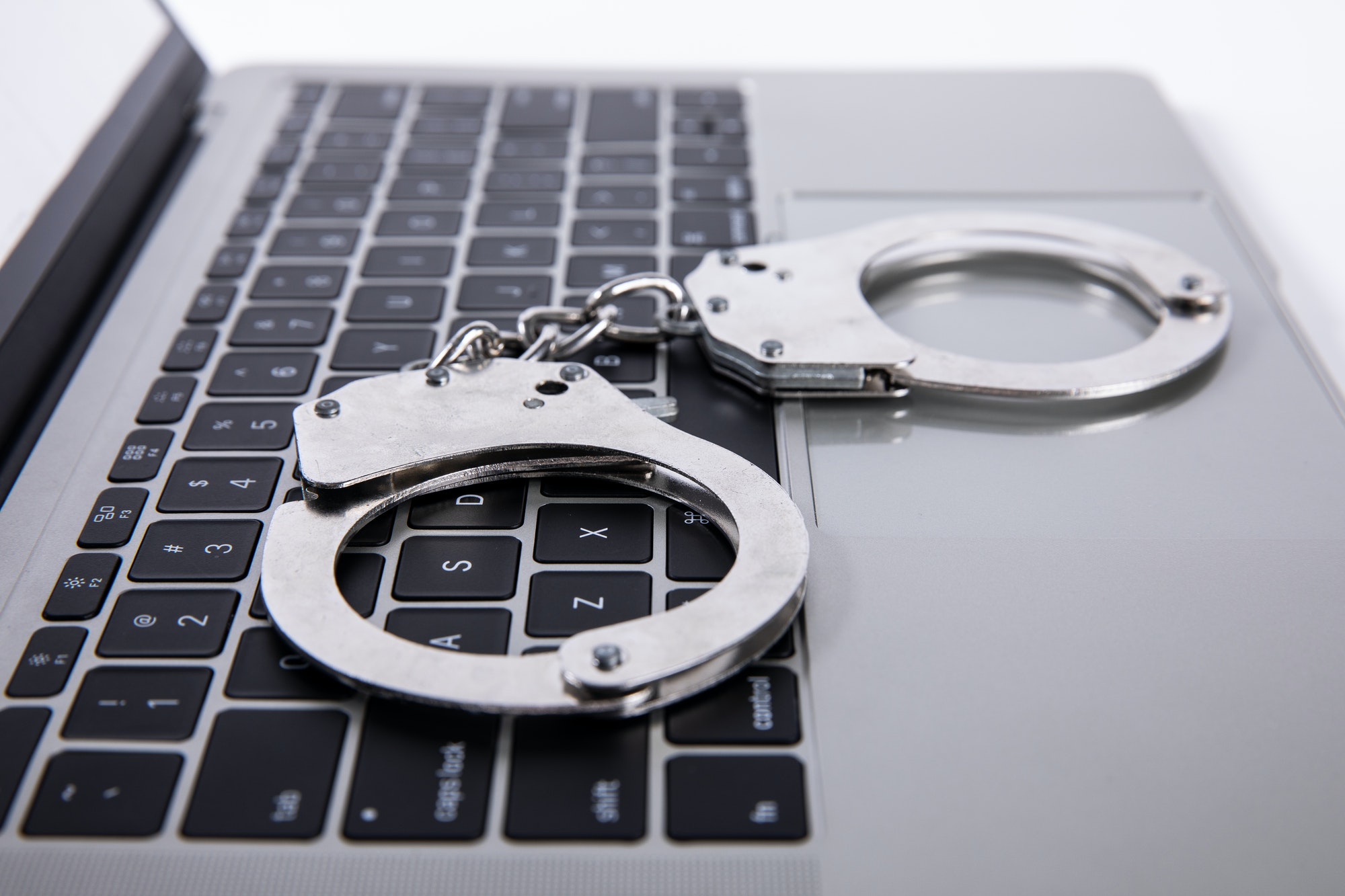 Closeup shot of handcuffs lying on laptop keypad - online crime concept